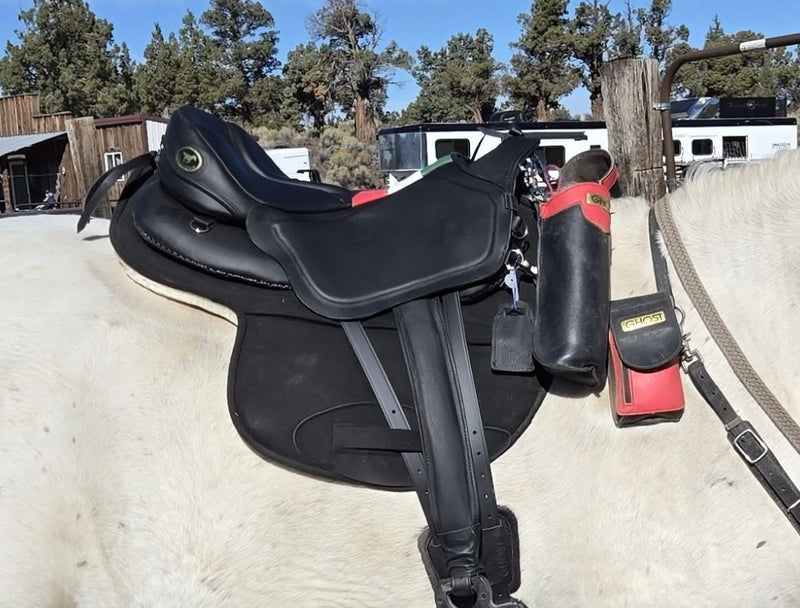 Sella da equitazione Ghost nera senza appoggi, equipaggiata con porta bottiglia e porta cellulare laterali rossi e neri su un cavallo grigio.