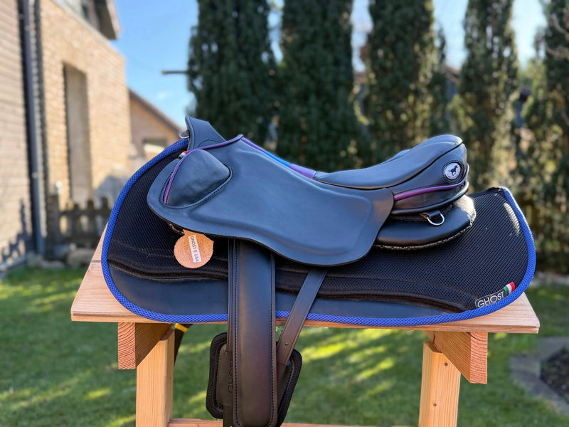 Sella da equitazione Ghost modello Endurance in pelle nera con profilatura viola, completa di quartieri stile USA e posizionata su un sottosella sagomato nero con bordo blu elettrico.