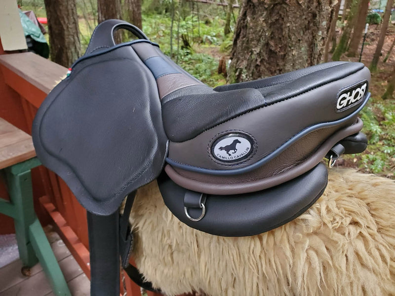 Sella da equitazione Ghost Endurance di tre quarti, in pelle nera e marrone con finiture e profili blu, completa di logo del brand e posizionata su un supporto in ecopelle/lana.