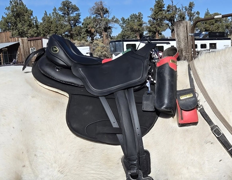 Sella da equitazione Ghost per endurance nera con accessori e borse laterali rosse e nere montata su un cavallo grigio.