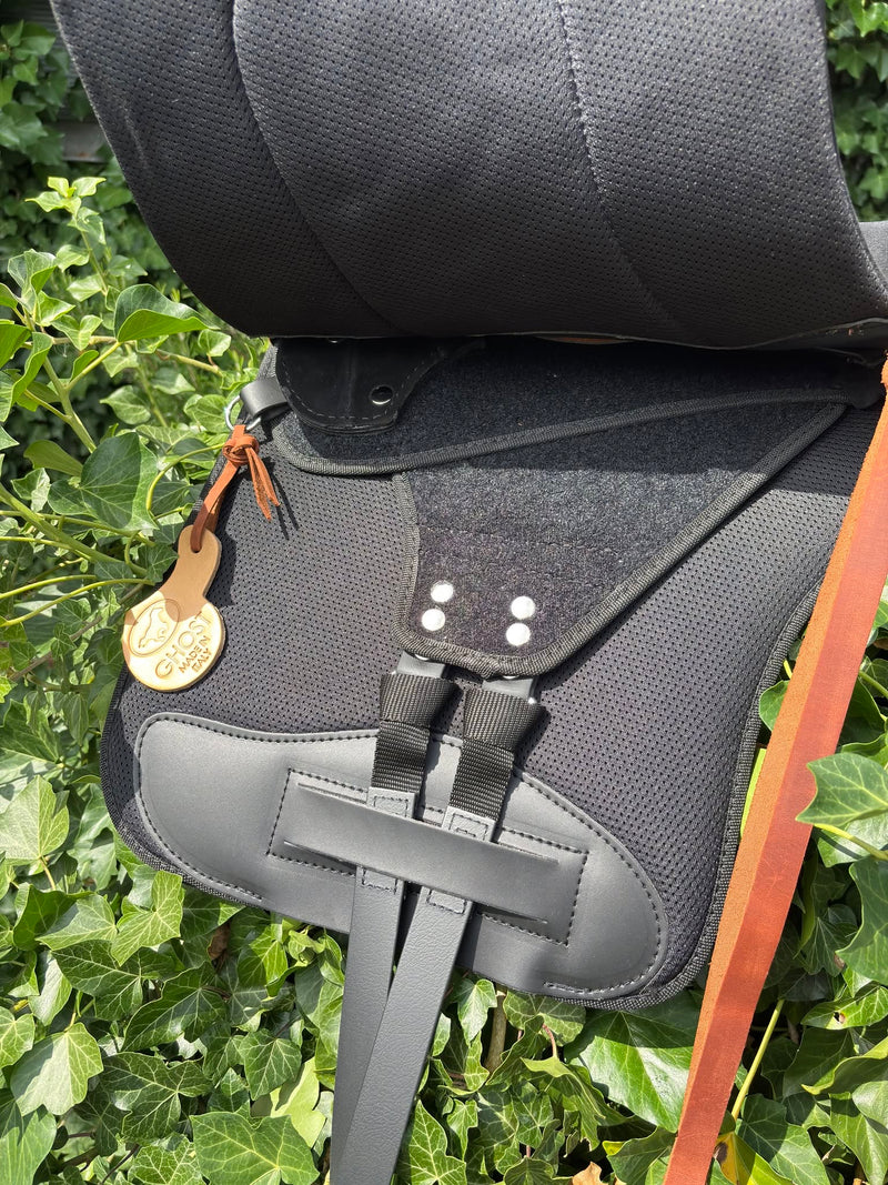 Sella Ivoska Rigging nera, dettaglio laterale con texture, fibbie e targhetta logo, sfondo foglie verdi